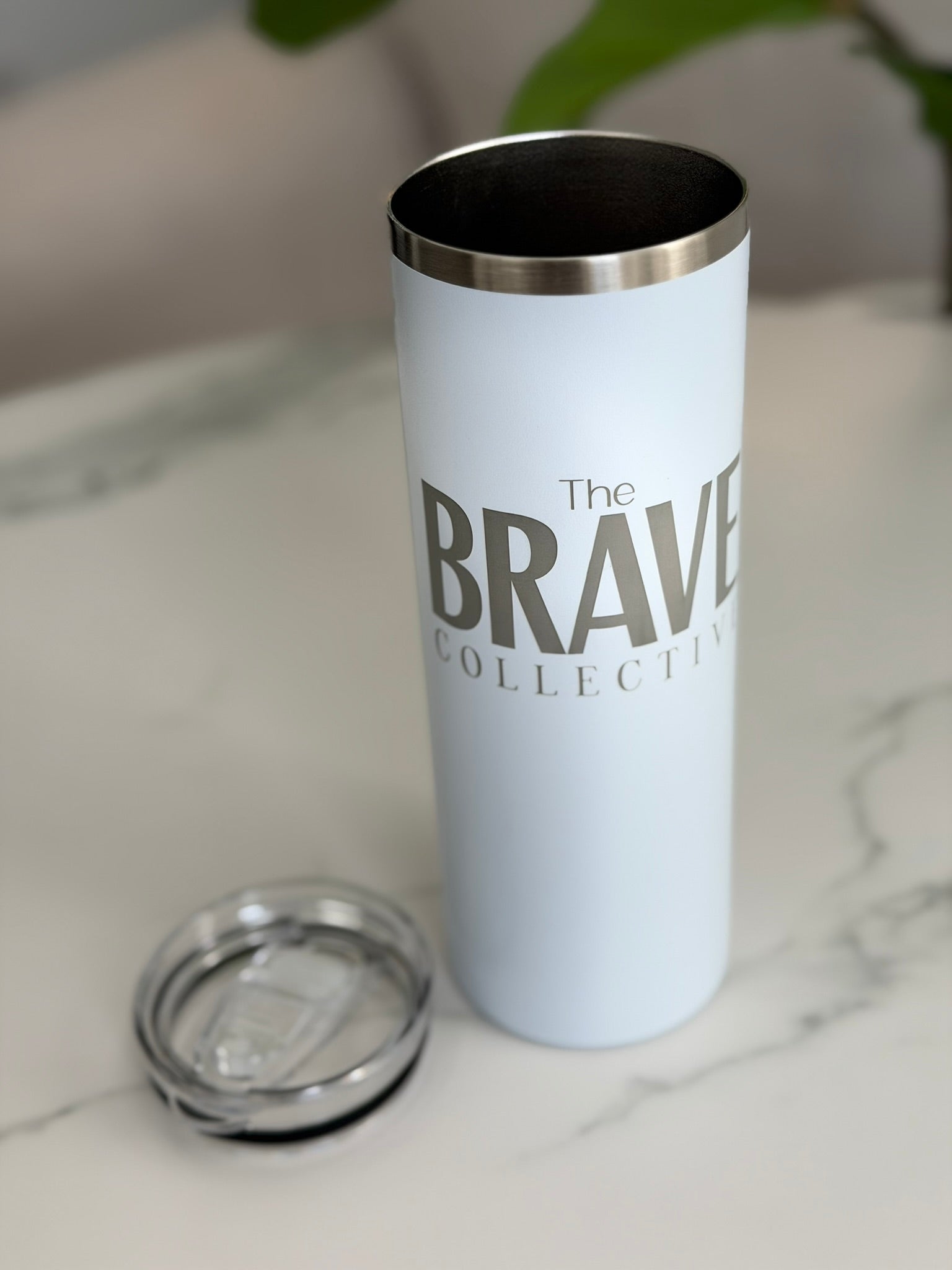 White tumbler with 'The Brave Collective' branding on a marble surface.