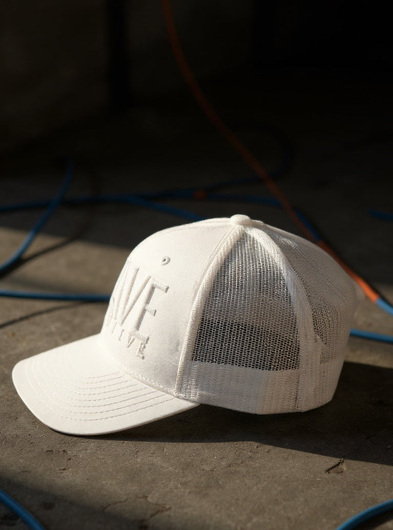 White cap with mesh back on a dark surface with blue and orange cables.