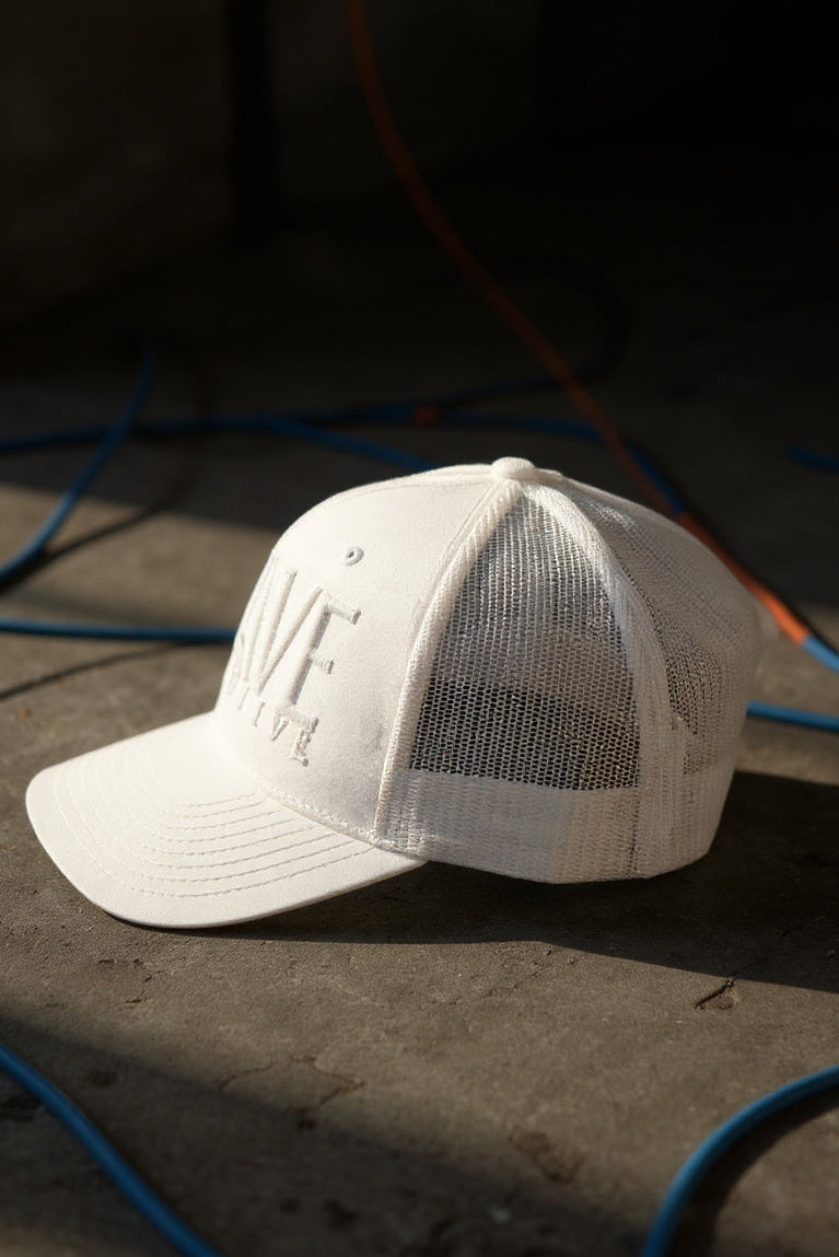 White cap with mesh back on a dark surface with blue and orange cables.