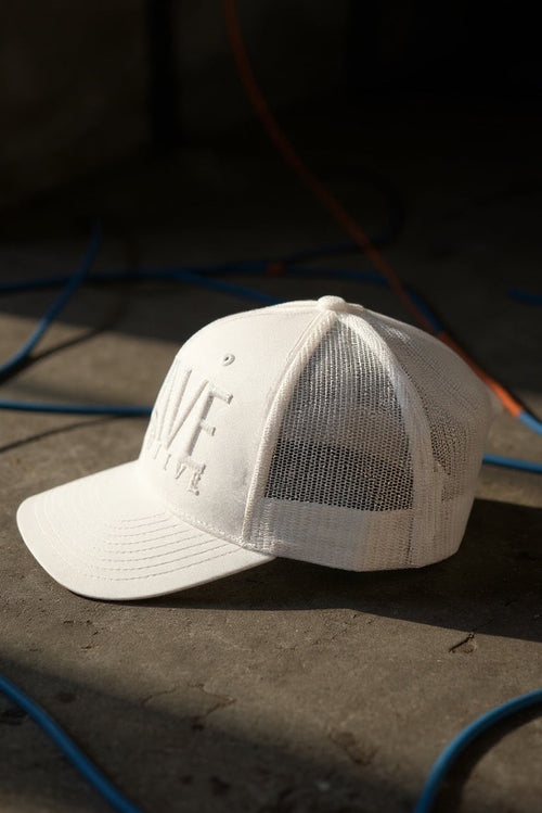 White cap with mesh back on a dark surface with blue and orange cables.